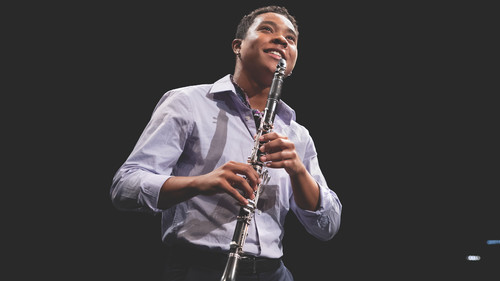 A smiling student is on stage holding a clarinet and poised to begin playing