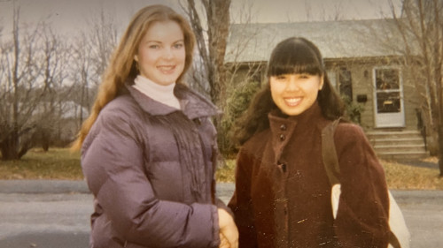 Ana Valdes Lim and Marcia Cross, dressed in warm winter coats, pose for a photo in front of a suburban house