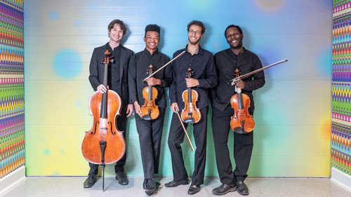 The Renaissance Quartet posing for a professional photo; they are dressed in "concert black" attire and hold their instruments and behind them is a bright, multicolored background