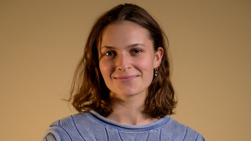 Headshot of Flora Ferguson against a neutral background. She is smiling and wears a lavender knit sweater