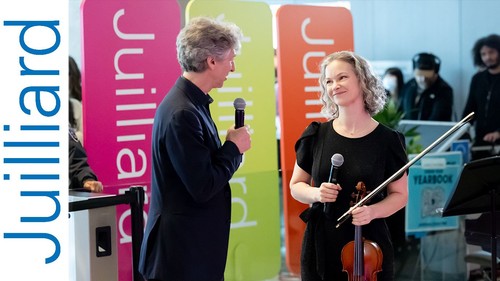man holding a microphone speaking to a woman holding a violin