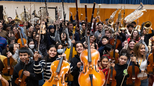 large group of young smiling students holding up stringed instruments