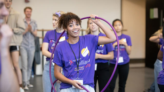 Younger woman happily participating in group activity holding hoola hoop over her shoulder