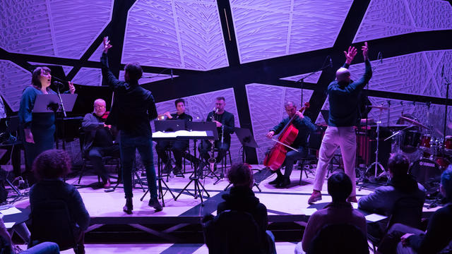 A vocal and instrumental performance in a contemporary looking concert hall with compelling violet lighting on the stage